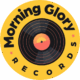 Logotyp för "Morning Glory Records" med en svart vinylskiva med orange och gula färger på en gul bakgrund, omgiven av varumärkesnamnet i fet svart text.